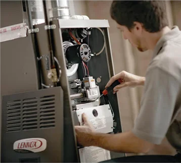 A technician is servicing an indoor Lennox furnace, with advanced furnace replacement services.