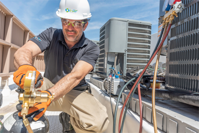 A technician in a hard hat and safety goggles services an air conditioning unit on a rooftop, using a gauge and tools as part of a home improvement project.