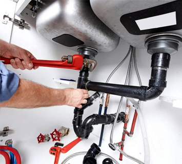 Plumber using a wrench to work on sink pipes beneath a kitchen sink as part of a home improvement project.