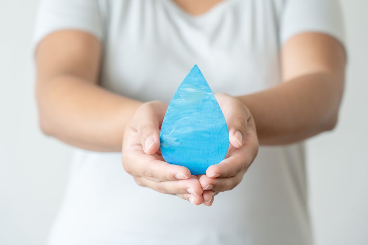 Hands holding a blue water drop-shaped object, symbolizing efficiency and sustainability, with a soft background, reminiscent of advanced hot water recirculation systems.