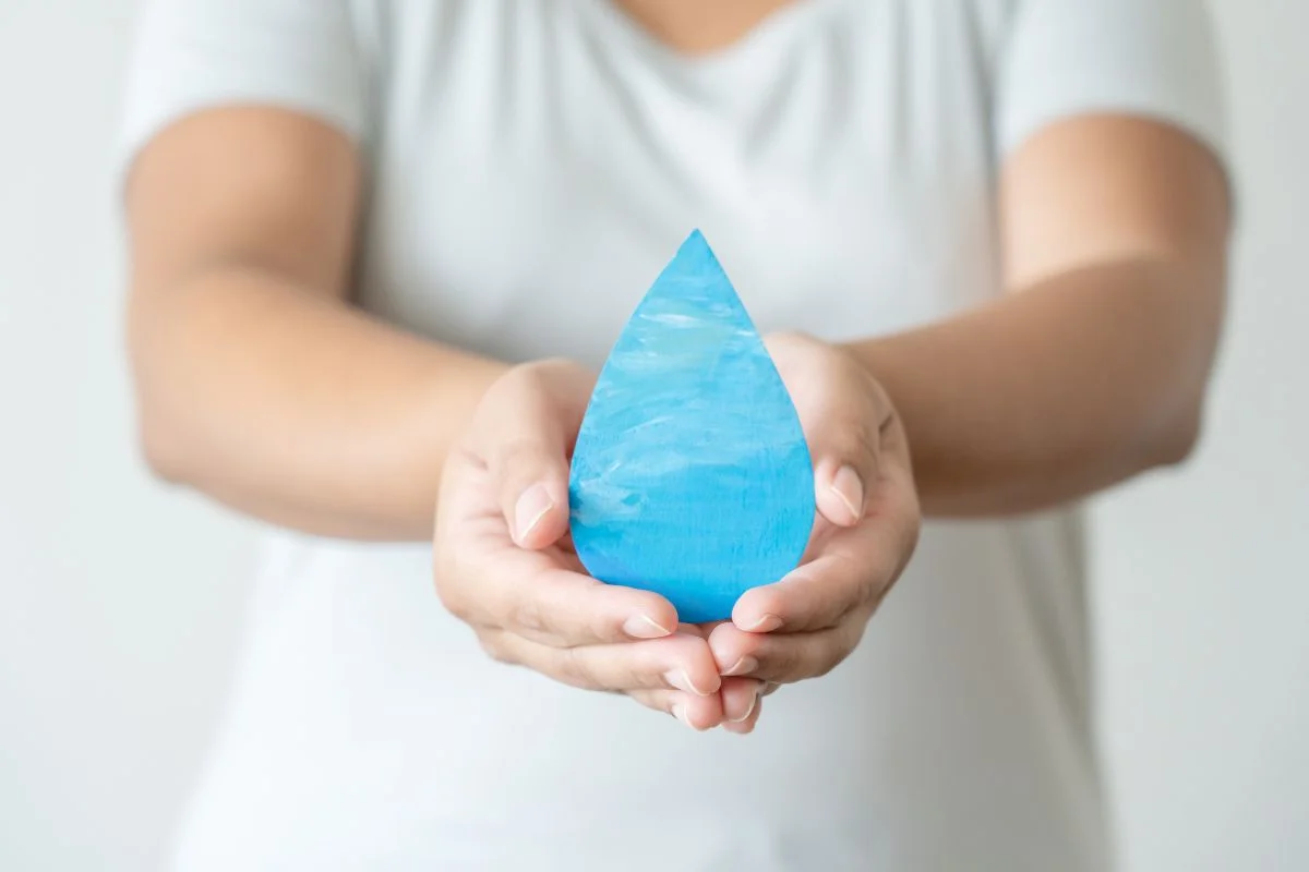 Hands holding a blue water drop-shaped object, symbolizing efficiency and sustainability, with a soft background, reminiscent of advanced hot water recirculation systems.