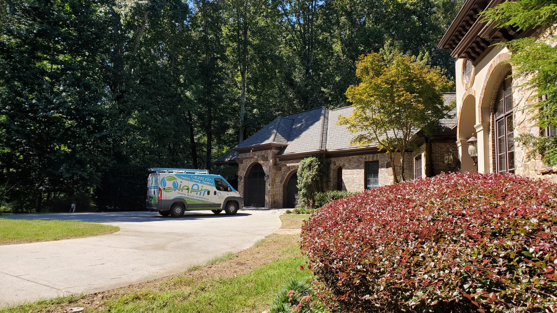 A service van parked in front of a large house with lush greenery and a clear blue sky.