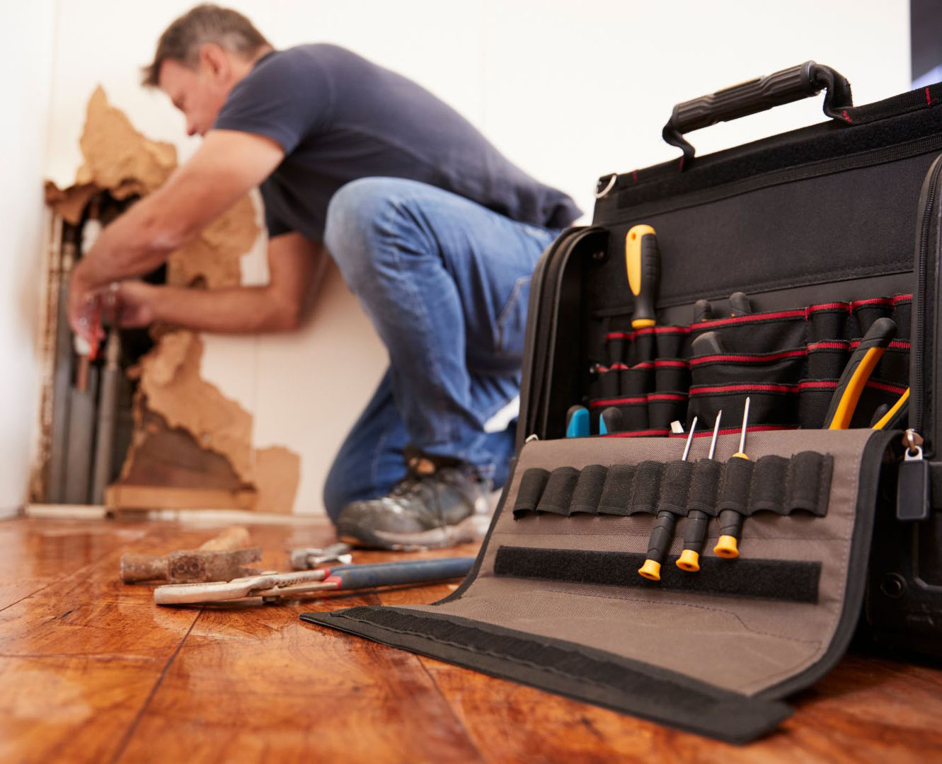 A plumber performing plumbing repair on broken pipes next to a tool bag with various tools spread out on the floor.