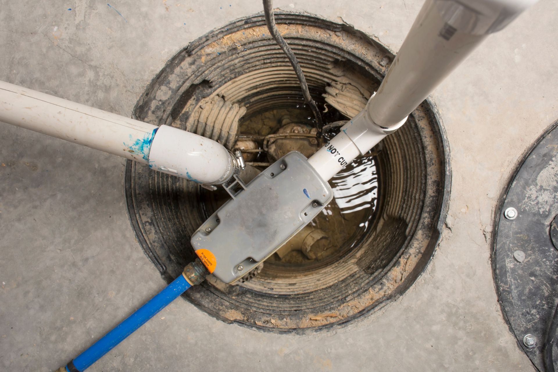 A utility space with pipes and electrical components in a round opening on the floor, partially filled with water, showcases the need for expert plumbing services.