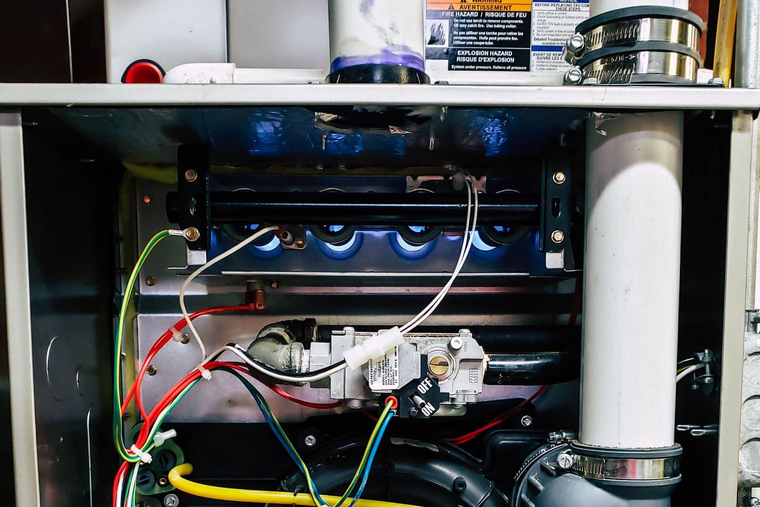 Close-up of the internal components of a gas furnace, showing wires, tubes, and a blue flame burner in operation; ideal for diagnosing furnace repair issues.