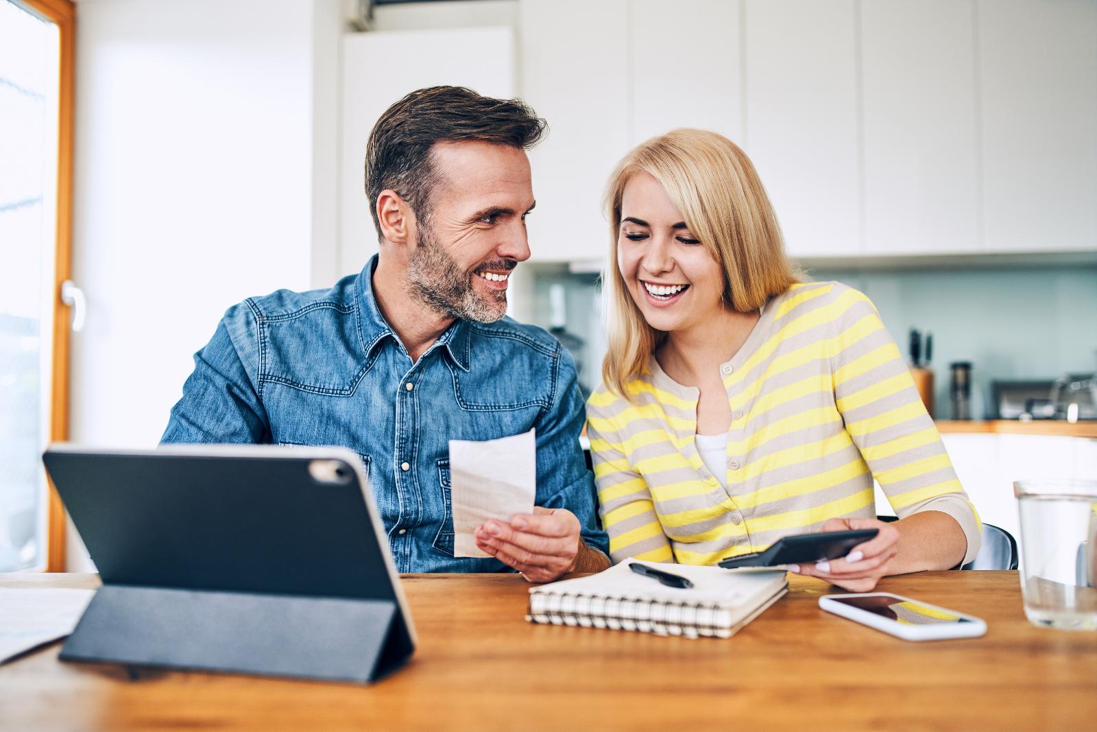 A man and woman at a table working together, looking at documents with a tablet, notebook, and smartphone in front of them, discussing financing options.