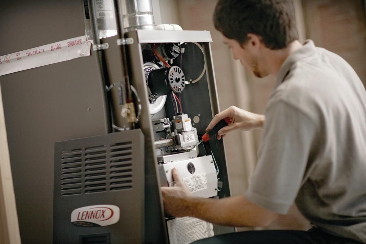 A technician providing HVAC services is repairing or inspecting an indoor furnace unit, labeled "Lennox," in a residential setting.