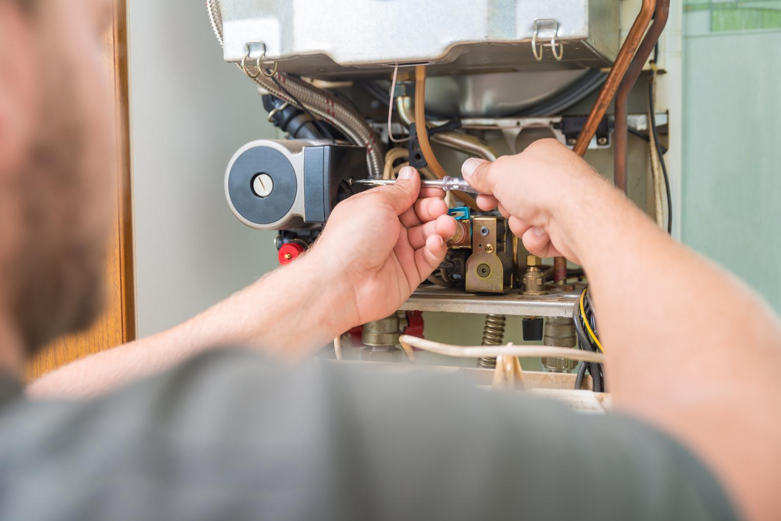 A technician is using a wrench to repair a complex network of pipes and wires in industrial equipment, focusing on furnace repair.