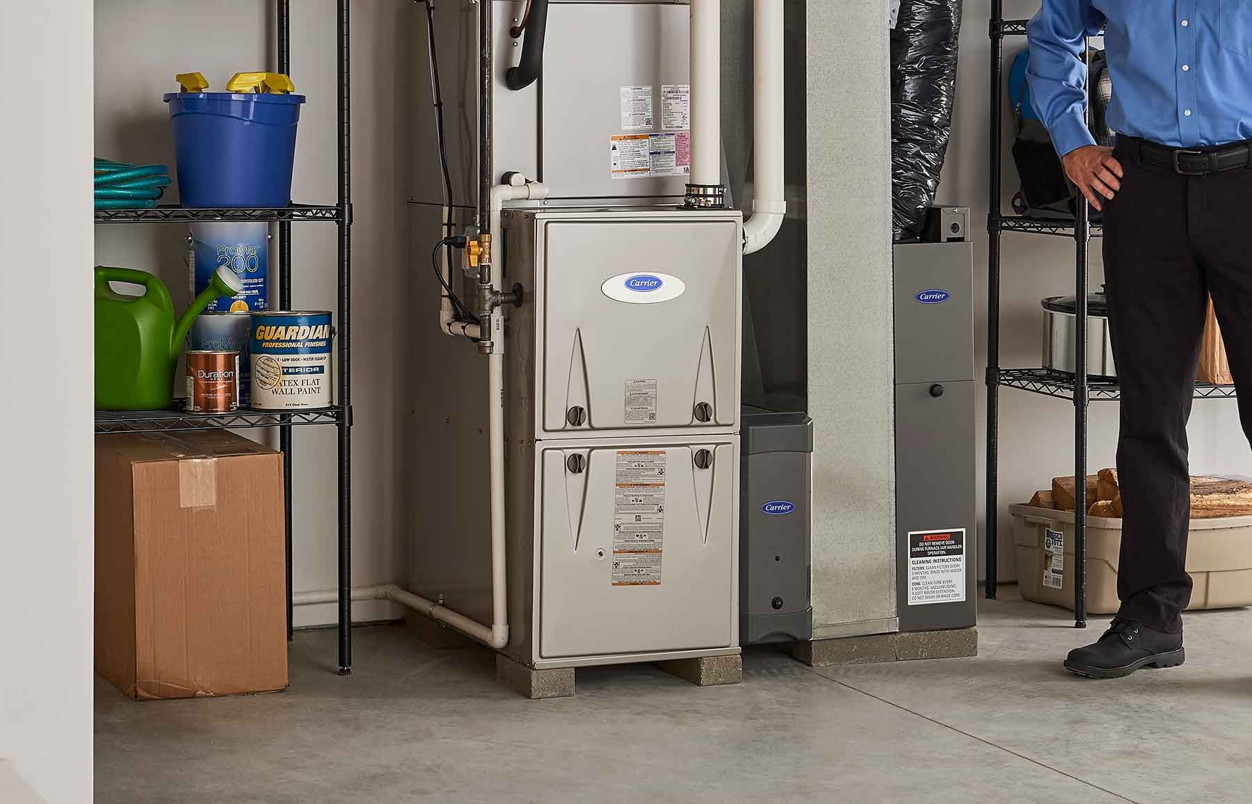 A well-organized home utility room features a furnace, shelves holding various supplies, and a person performing furnace repair beside the equipment.