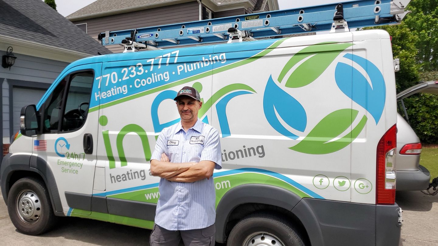 A man in a uniform stands in front of a service van labeled with "Heating, Cooling, Plumbing" and company contact details. A ladder is secured on top of the van, ready for air conditioning tune-ups.