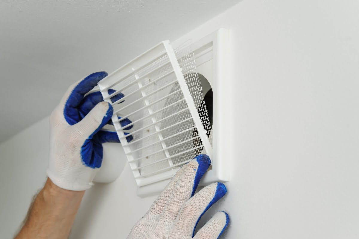 A person wearing white and blue gloves installs or adjusts a white vent cover on a wall, ensuring optimal performance for an affordable air conditioning system.