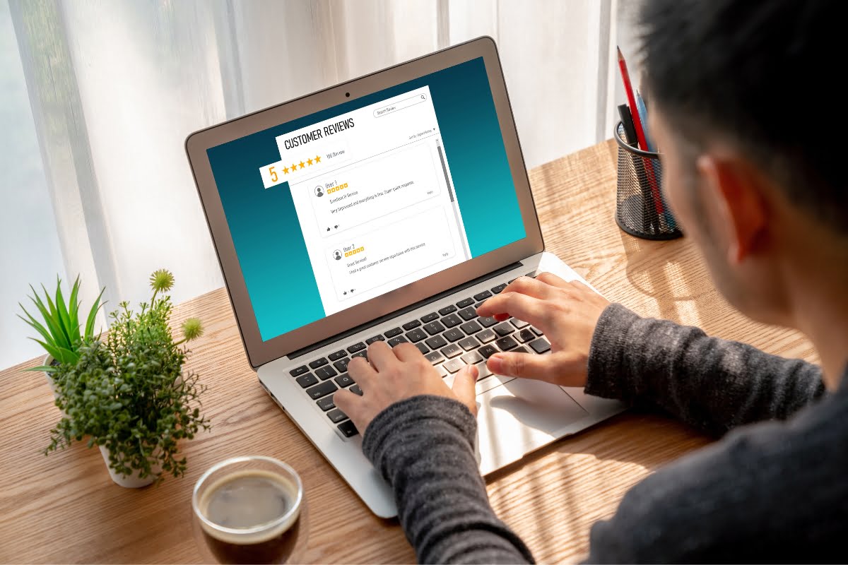 Person using a laptop to read customer reviews displayed on the screen, with a coffee cup, potted plant, and pen holder on the wooden desk nearby, ensuring they are choosing the right HVAC contractor.