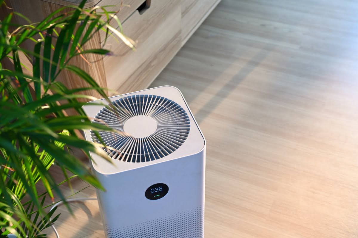 A white air purifier with a digital display showing "036" is placed on a light wood floor next to a green potted plant, highlighting the latest HVAC trends in modern home design.