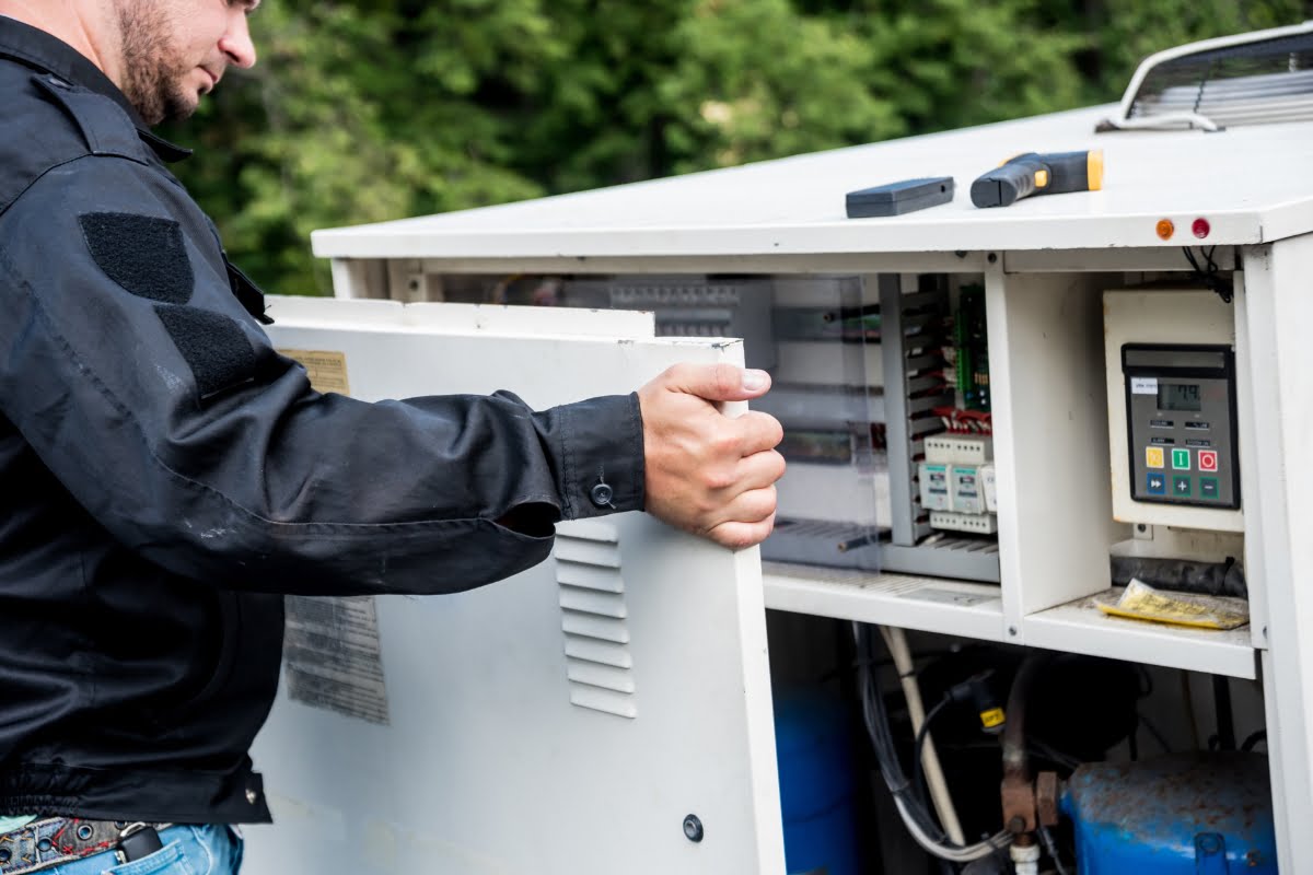 A person in a black jacket opens the door of a control panel that contains various circuit components and a digital display, reflecting the latest HVAC trends. Tools are visible on top of the panel.