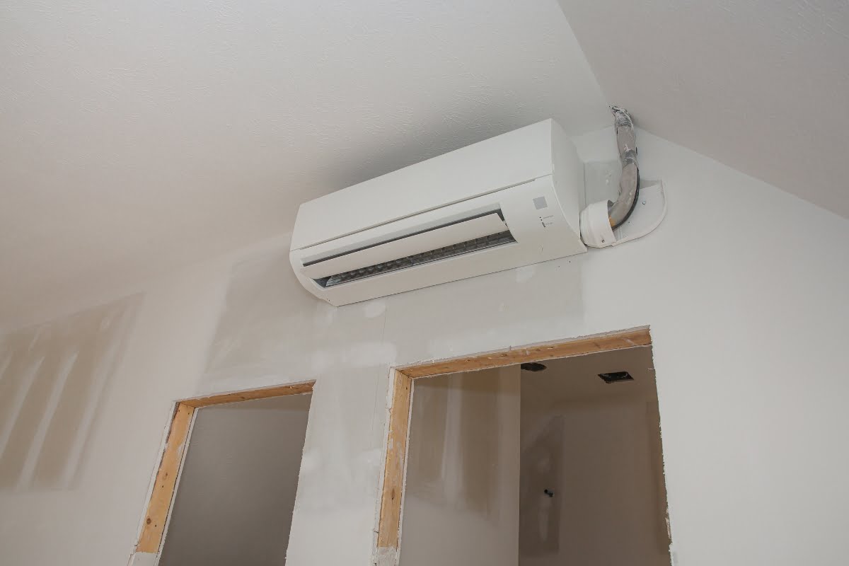 A wall-mounted air conditioning unit, reflecting the latest HVAC trends, is installed above two doorways on an unfinished interior wall.