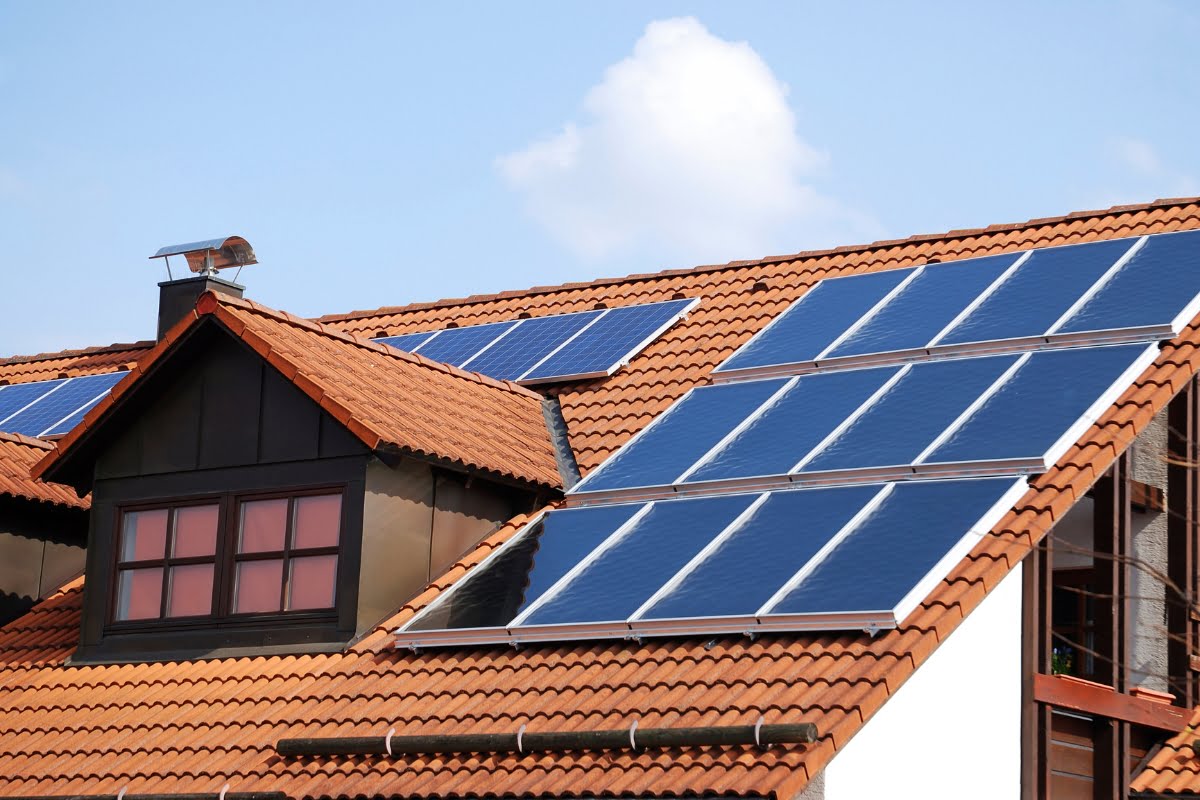 A house with orange roof tiles boasts multiple solar panels on its roof under a partly cloudy sky, embracing the latest HVAC trends.