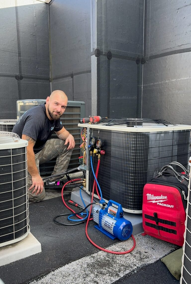 A person kneels beside HVAC units on a rooftop, meticulously working with tools and equipment as part of routine maintenance plans, featuring a red Milwaukee tool bag and a blue air pump.