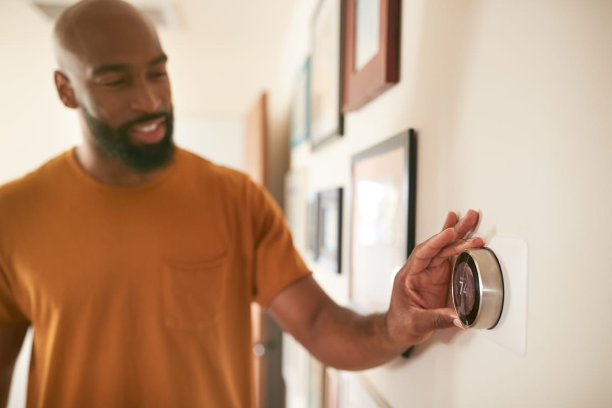 A person in a brown shirt adjusts a modern digital thermostat, seamlessly integrating it into the smart HVAC system of their home.