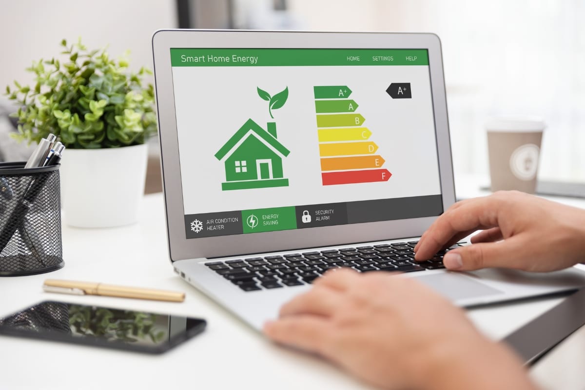 A person uses a laptop displaying a smart home energy efficiency interface, featuring a green house icon and an energy rating chart, seamlessly integrating smart HVAC systems for optimal performance.