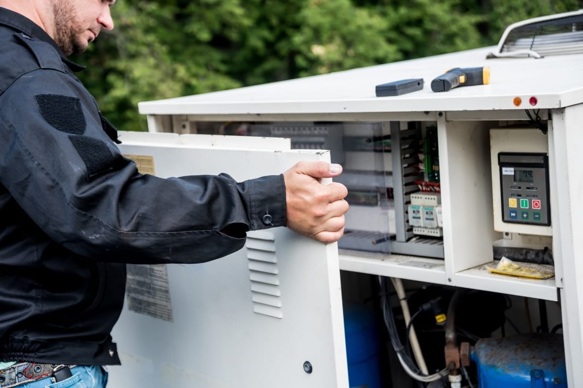 Person in a black jacket opening a control panel outdoors, revealing electronic components and a display, providing an insightful glimpse into expert HVAC maintenance tips.