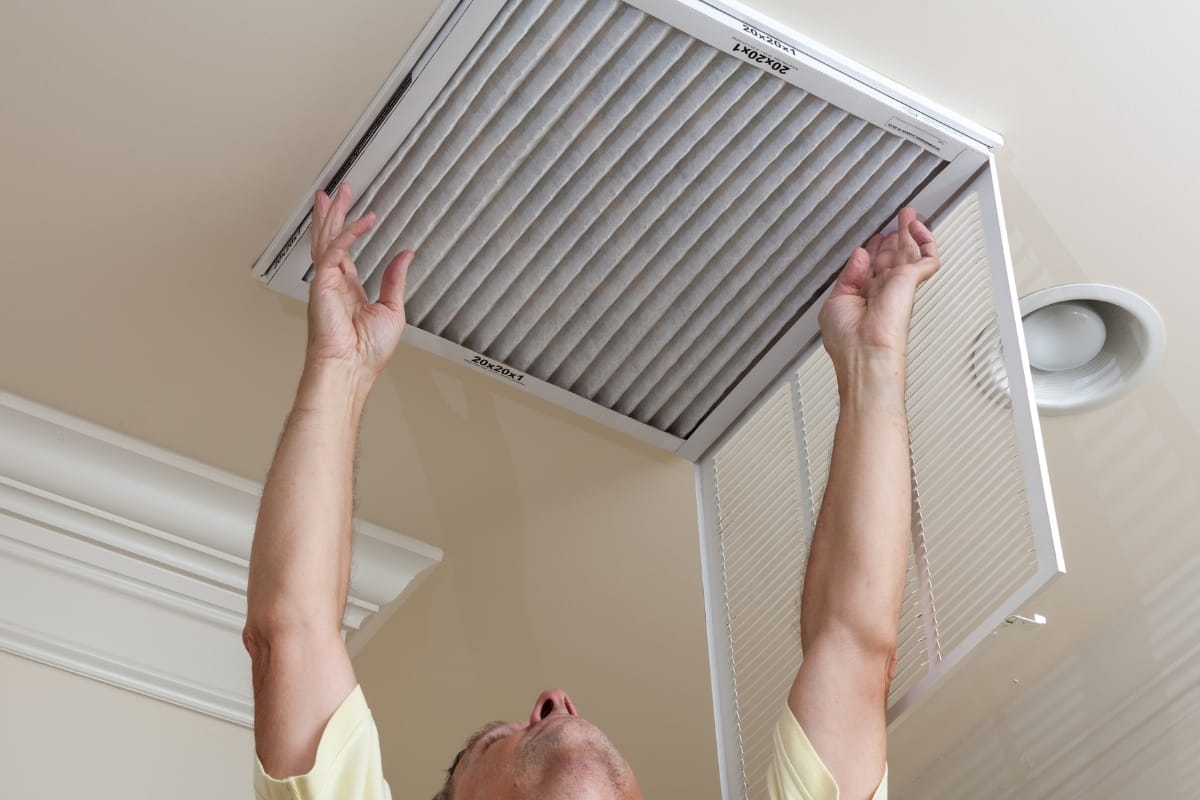 A person is expertly changing an air filter in a ceiling vent, showcasing effective HVAC maintenance tips to ensure optimal air quality and system efficiency.