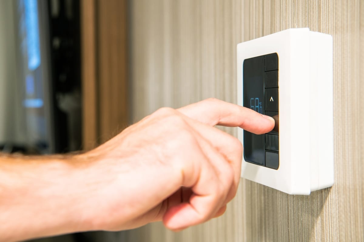 A hand carefully adjusts the settings on a modern thermostat mounted on a wall, showcasing smart HVAC maintenance tips for optimal home comfort.