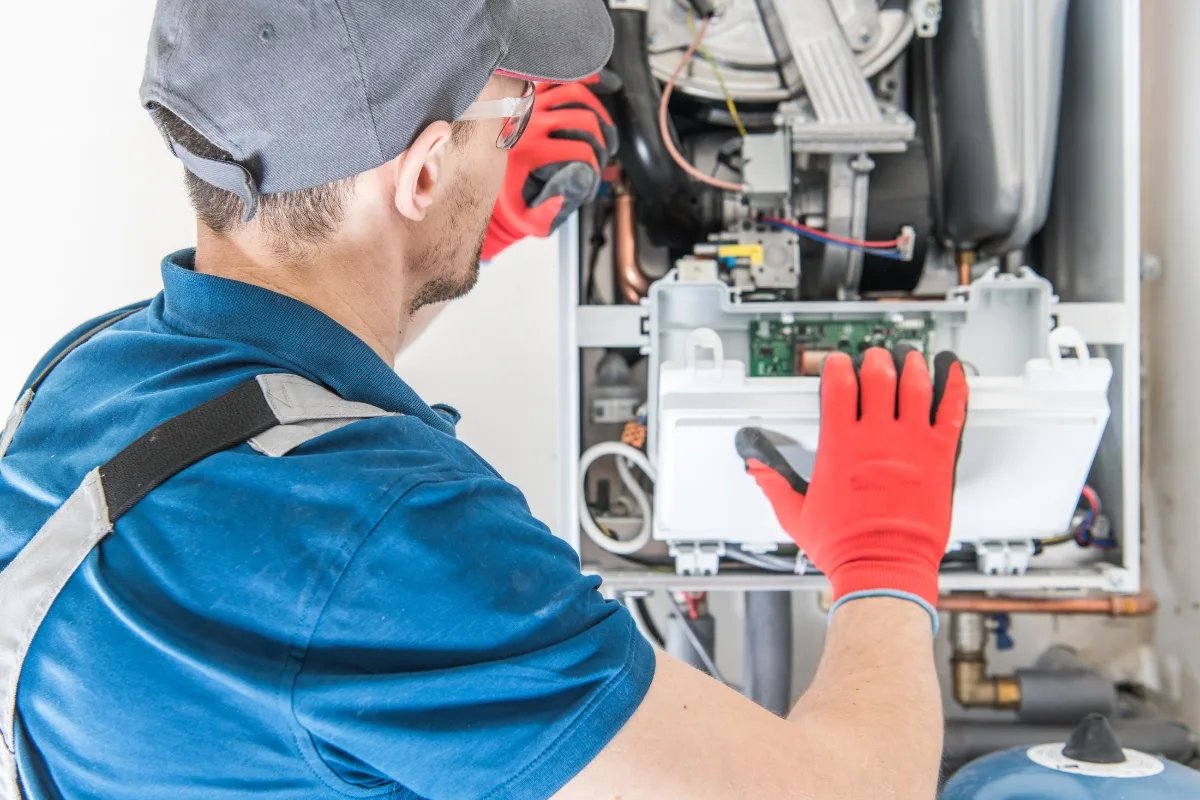 A technician in a blue uniform and red gloves works on a boiler, inspecting internal components to identify common furnace problems.