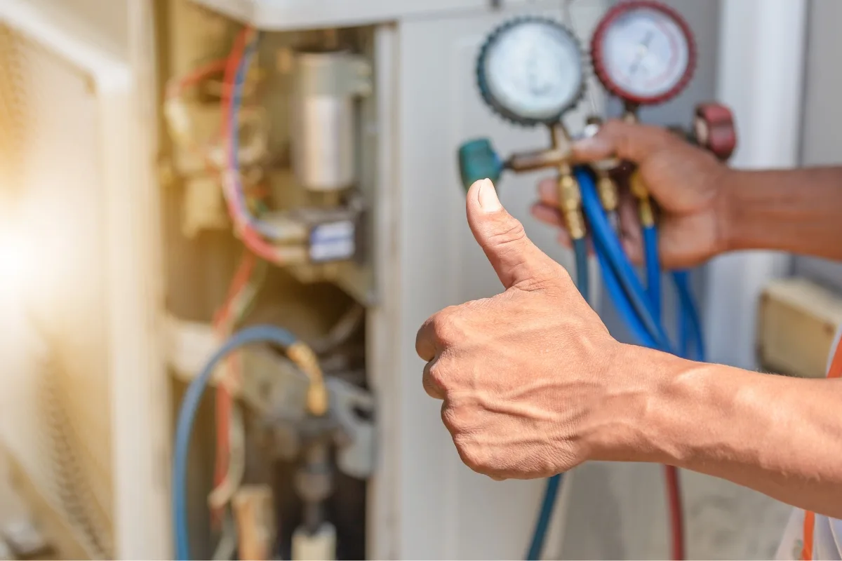 A person gives a thumbs up while holding air conditioning gauges, expertly checking the system's pressure for any heat pump issues.