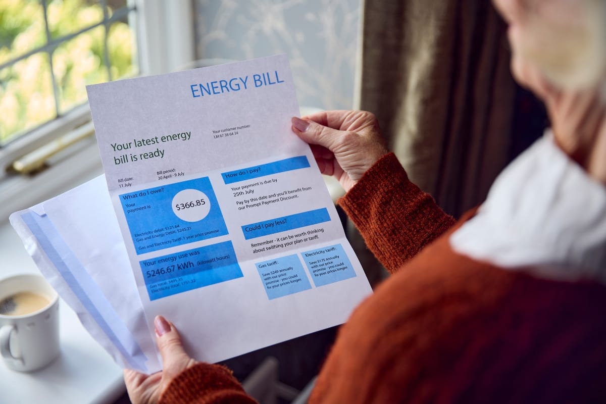 A person holds an energy bill showing a total of $366.85, with usage details and payment instructions, next to a window and cup of coffee—HVAC repair signs may explain the unexpectedly high costs.
