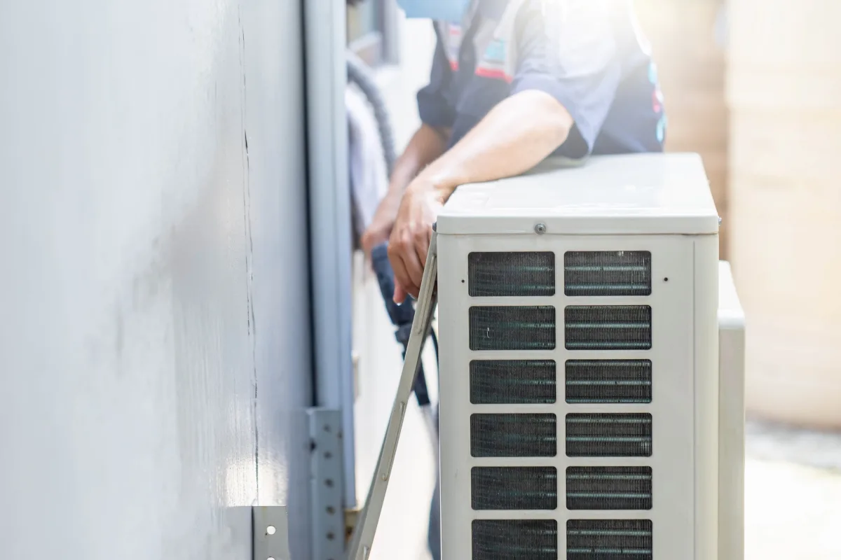 A technician is servicing or installing an outdoor HVAC system unit next to a building wall.