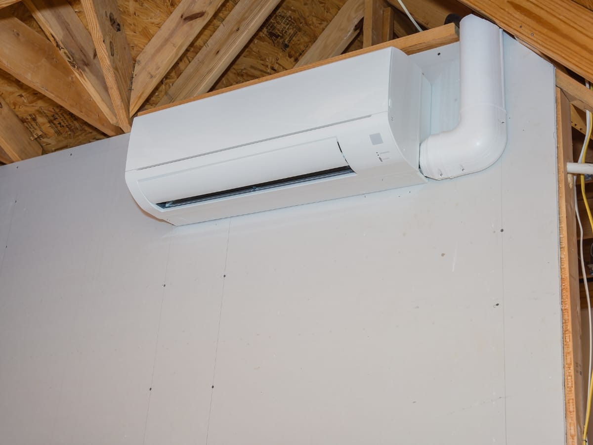 Wall-mounted ductless mini-split air conditioning unit installed on an unfinished interior wall with exposed wooden ceiling beams.