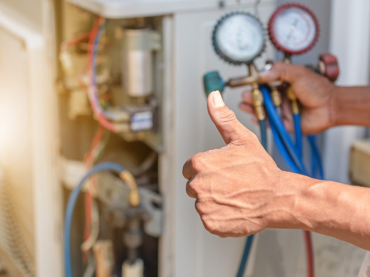 A person gives a thumbs up while checking air conditioning gauges next to open HVAC equipment during an HVAC tune-up.