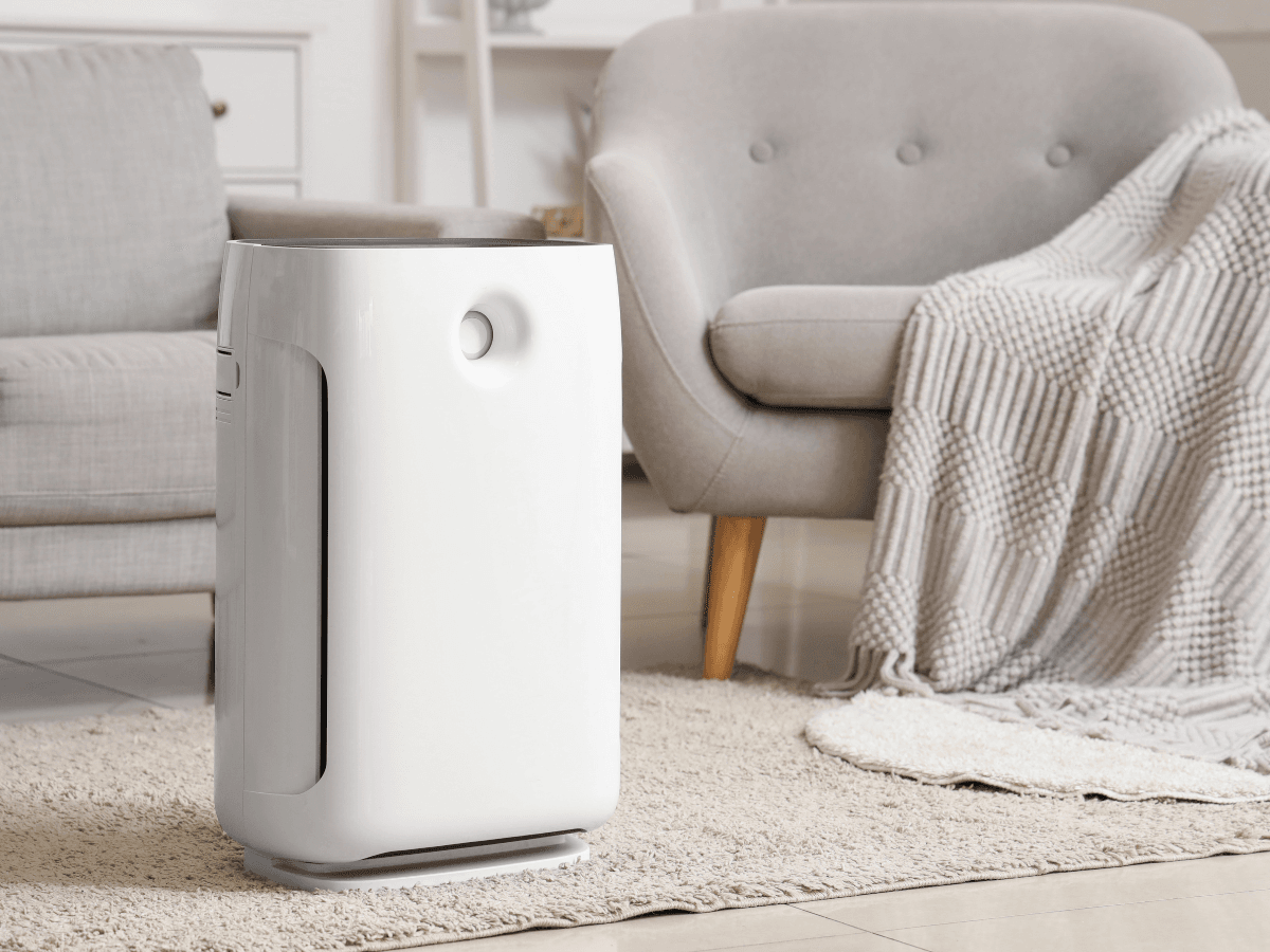 A modern white air purifier sits on a beige rug in a cozy living room with an armchair and a blanket in the background, offering a stylish solution for enhancing indoor air quality in Atlanta homes.