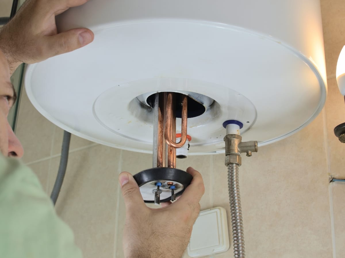 Person installing or repairing a heating element in the bottom of a tankless water heater mounted on a bathroom wall.