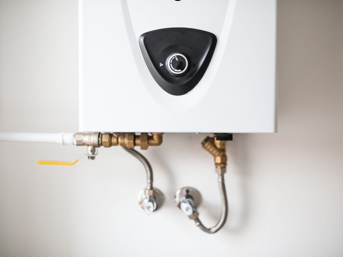Close-up of a modern wall-mounted tankless water heater with visible pipes and fittings attached underneath, showcasing the compact design typical of Tankless Water Heaters.