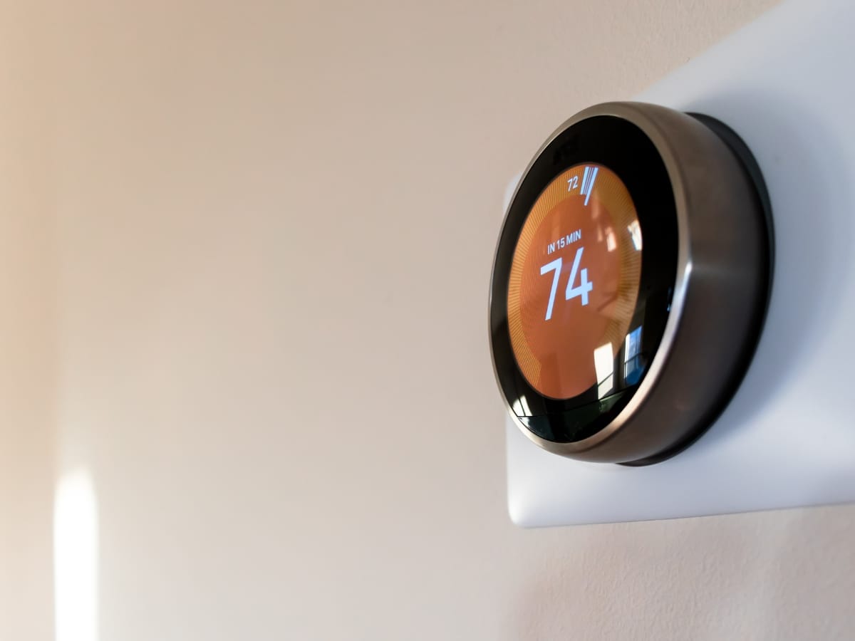 A smart thermostat mounted on a wall displays an indoor temperature of 74 degrees Fahrenheit, helping you reduce energy bills efficiently.