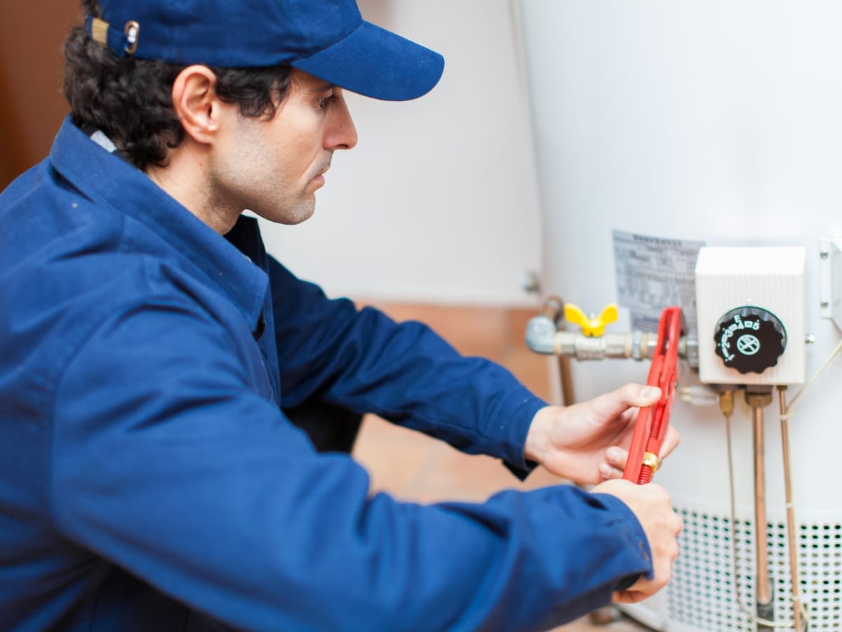 A technician in blue uniform uses a wrench to adjust a valve on a water heater, helping to optimize performance and reduce energy bills.
