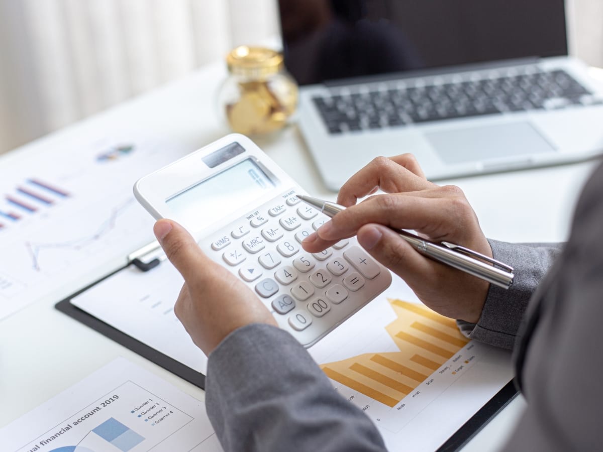 A person uses a calculator at a desk with financial charts, a laptop, and a clipboard displaying a bar graph—analyzing budgets for home renovation trends Atlanta homeowners are currently embracing.