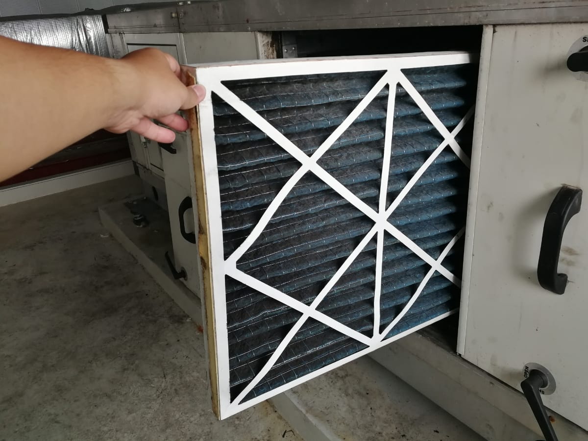 A person is removing a dirty air filter from an air conditioning unit for maintenance or replacement, ensuring the system remains allergy friendly HVAC.