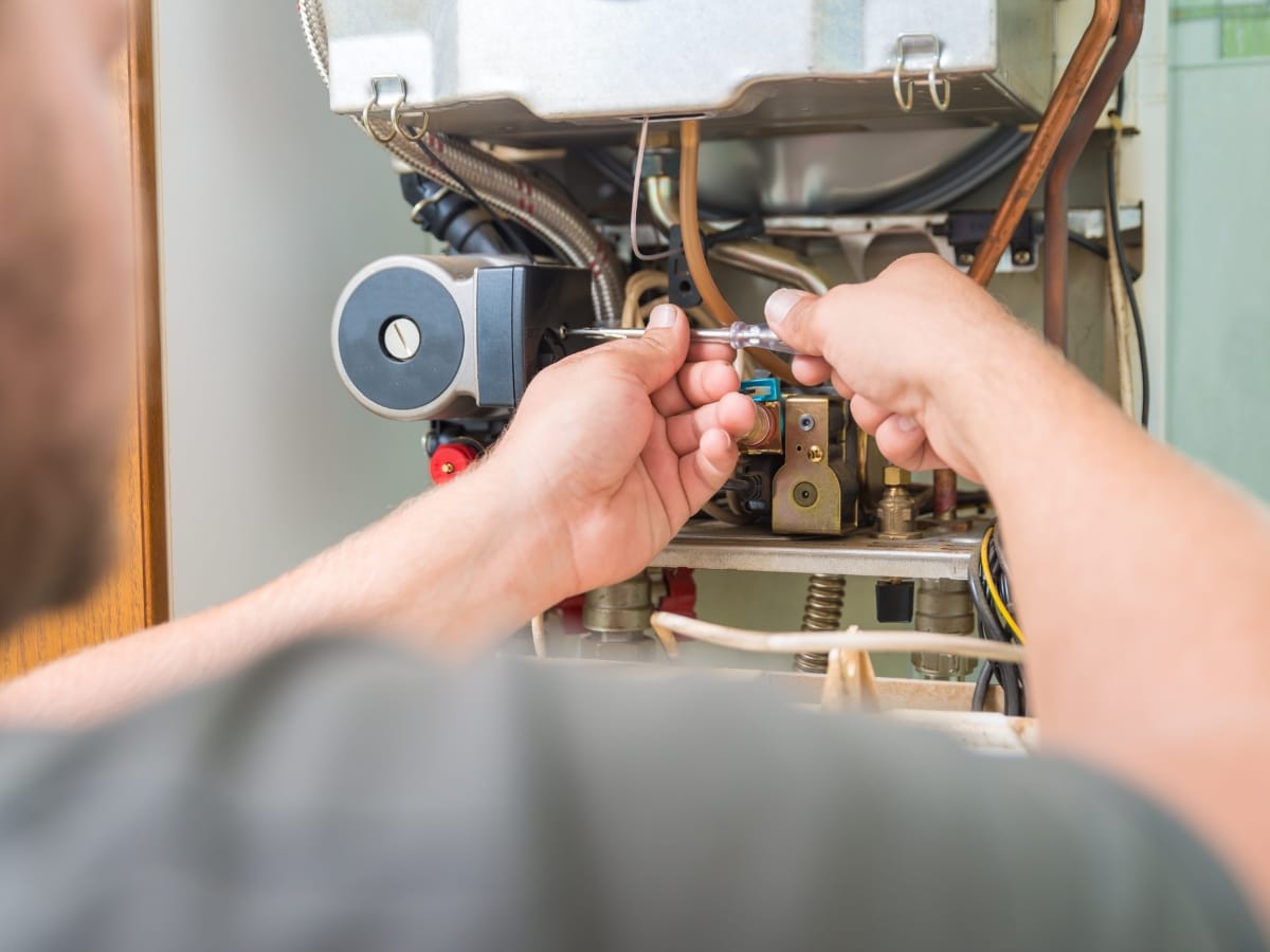 A person using tools to repair or maintain the internal components of a gas boiler or water heater, focusing on furnace troubleshooting for efficient operation.