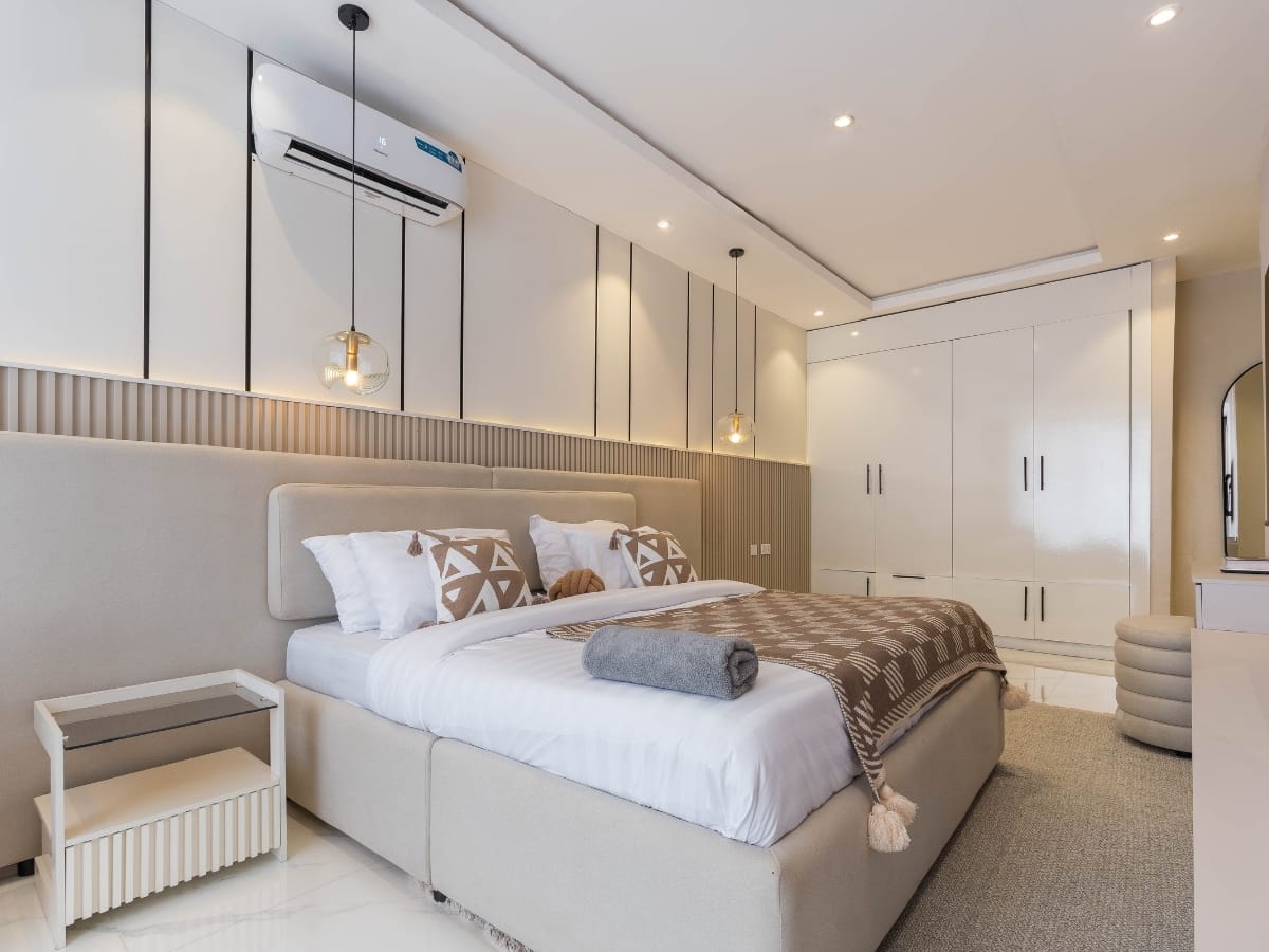 Modern bedroom with a large bed, neatly arranged pillows and blanket, built-in wardrobes, pendant lights, and a pet friendly HVAC wall-mounted air conditioner.