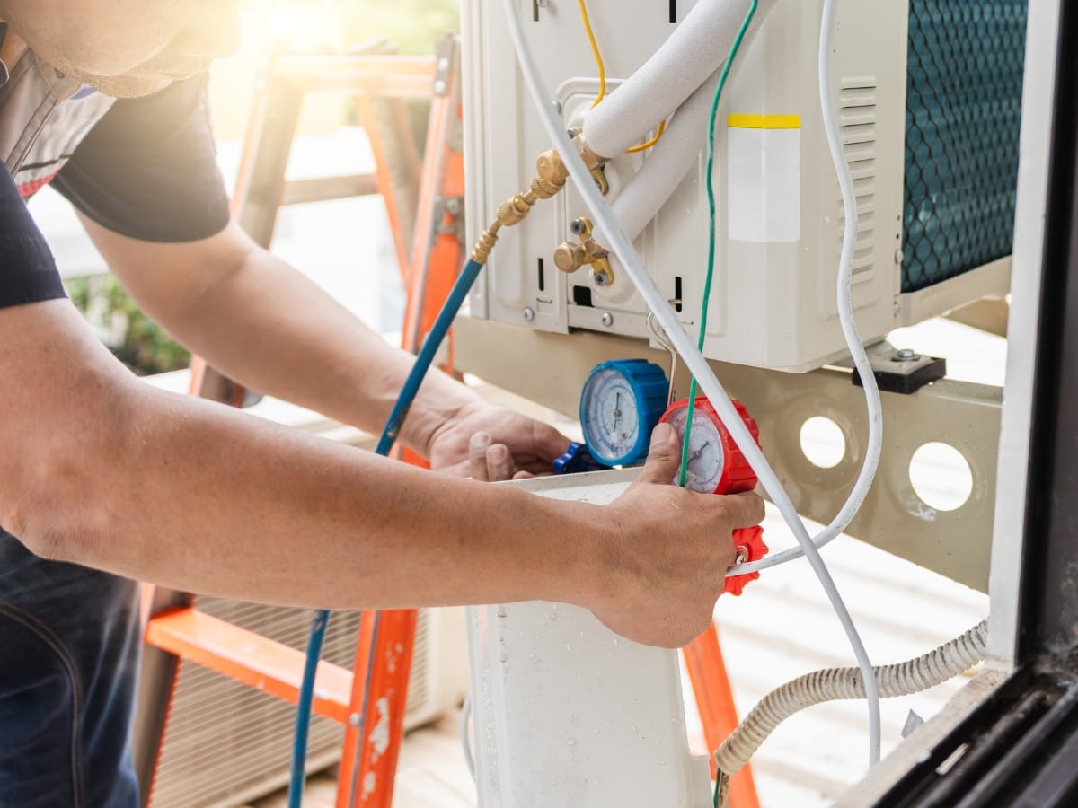A technician uses pressure gauges to check or repair a pet friendly HVAC air conditioning unit, with various wires and hoses attached to the system.
