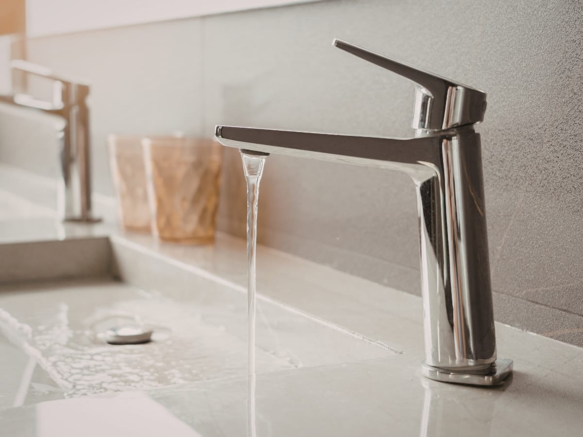 A modern chrome faucet with water running into a white sink, spilling over the edge onto the countertop—perfect for showcasing expert faucet repair installation services.