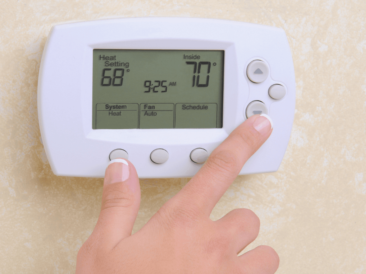 A hand presses a button on a digital thermostat, part of an energy-efficient HVAC system, displaying a heat setting of 68°F and an inside temperature of 70°F—helping to reduce climate impact.