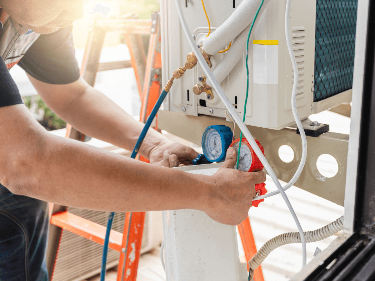 Person adjusting pressure gauges on an air conditioning unit during maintenance, with tools and equipment visible in the background—an essential step in maintaining home value and ensuring reliable HVAC performance.