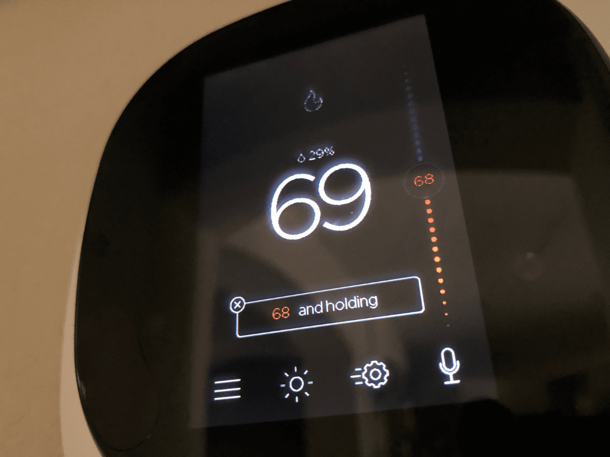 A smart thermostat display shows the temperature set at 69°F, with a status message reading “68 and holding.”.